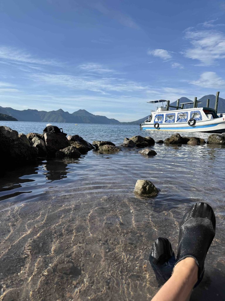 Feet in water shoes relaxing in the hot springs at Santa Catarina Palopó with boat and volcano views on Lake Atitlán