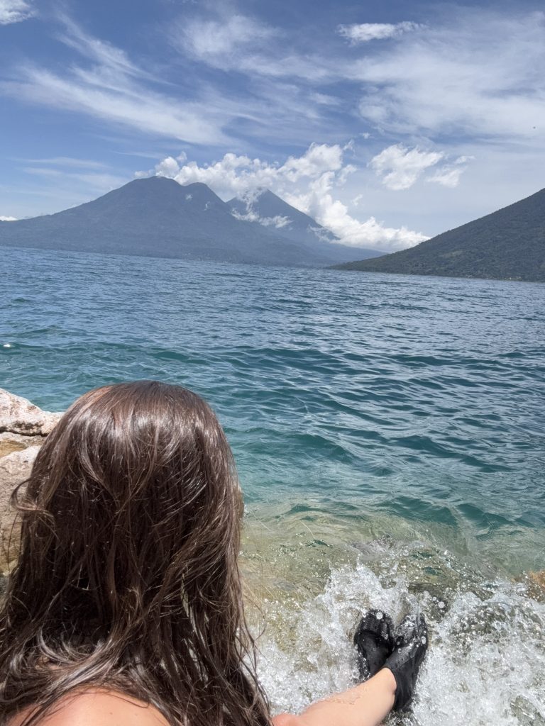 Woman in water shoes splashing in Lake Atitlán at Cerro Tzank’ujil with twin volcanoes in view
