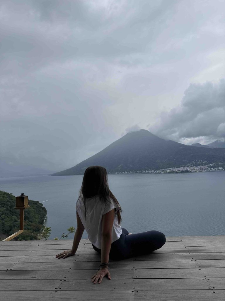 Solo female traveler sitting on the deck at Eagle’s Nest overlooking a cloudy Lake Atitlán during rainy season