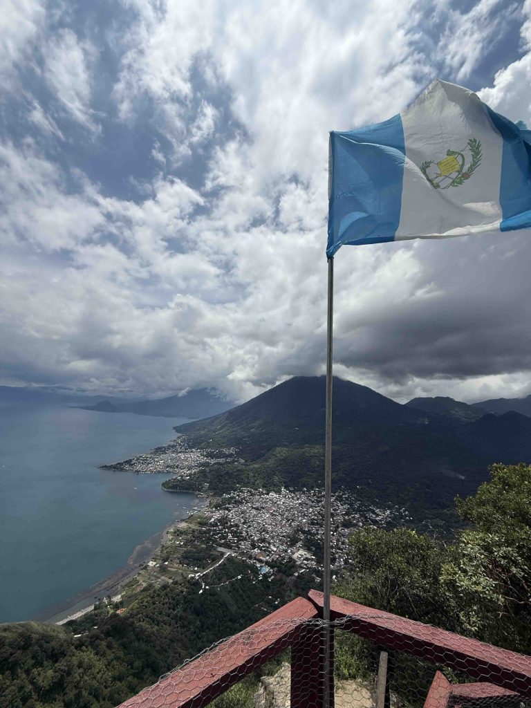 Guatemalan flag flying at the Indian Nose viewpoint with Lake Atitlán and volcanoes below
