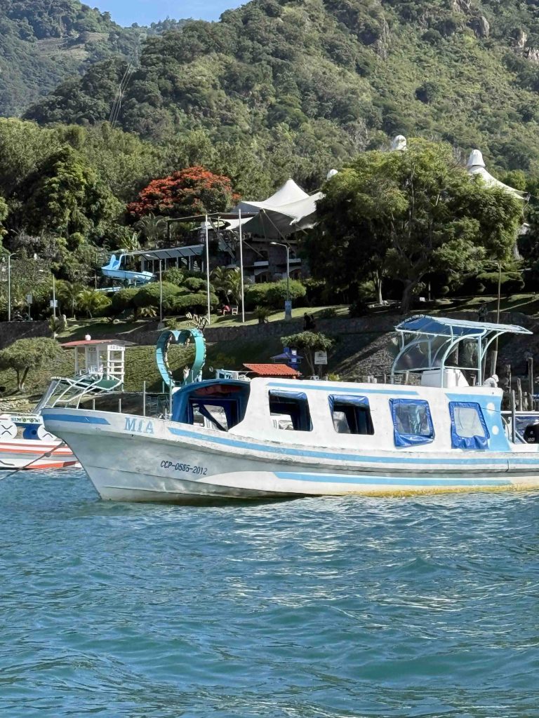 White and blue lancha boat on turquoise Lake Atitlán with green hills and hotel in the background