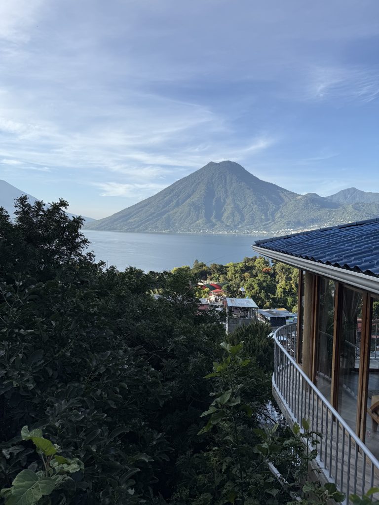 Morning view of San Pedro volcano rising over Lake Atitlán, framed by lush trees and rooftops from a terrace in San Marcos La Laguna.