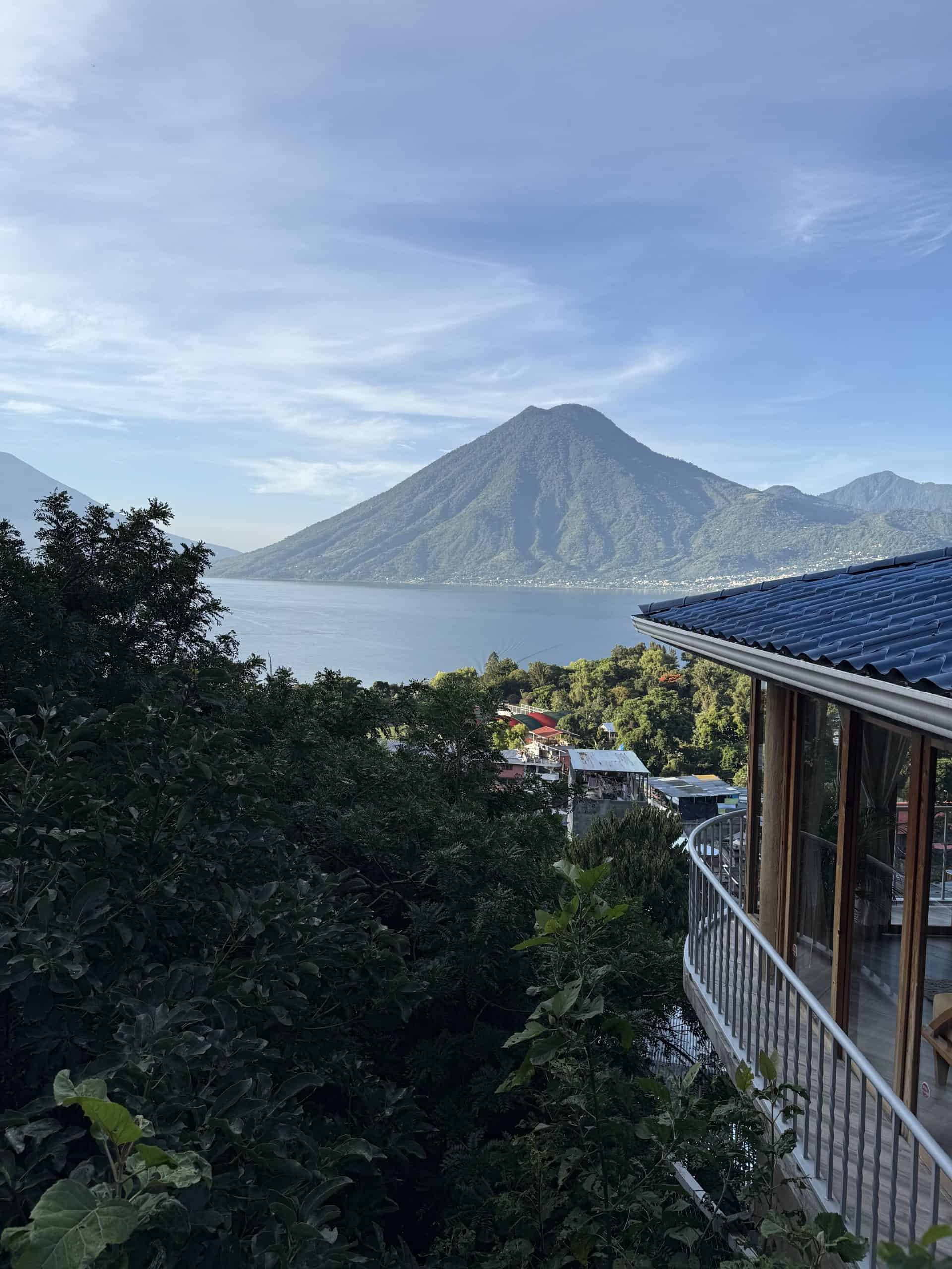 Morning view of San Pedro volcano rising over Lake Atitlán, framed by lush trees and rooftops from a terrace in San Marcos La Laguna.