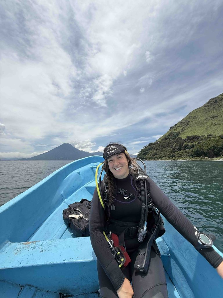 Scuba diver in wetsuit sitting on blue dive boat with volcano and Lake Atitlán in the background