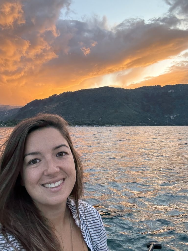Woman on Lake Atitlán with dramatic orange sunset clouds over the hills
