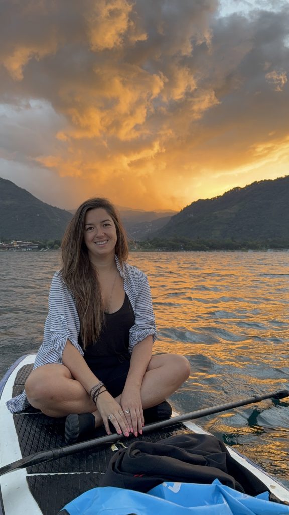 Woman sitting on a paddle board at sunrise on Lake Atitlán with fiery orange sky and mountains behind