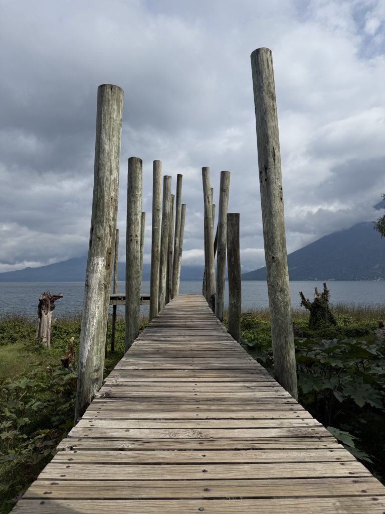 Wooden dock with tall posts leading out over Lake Atitlán under cloudy sky