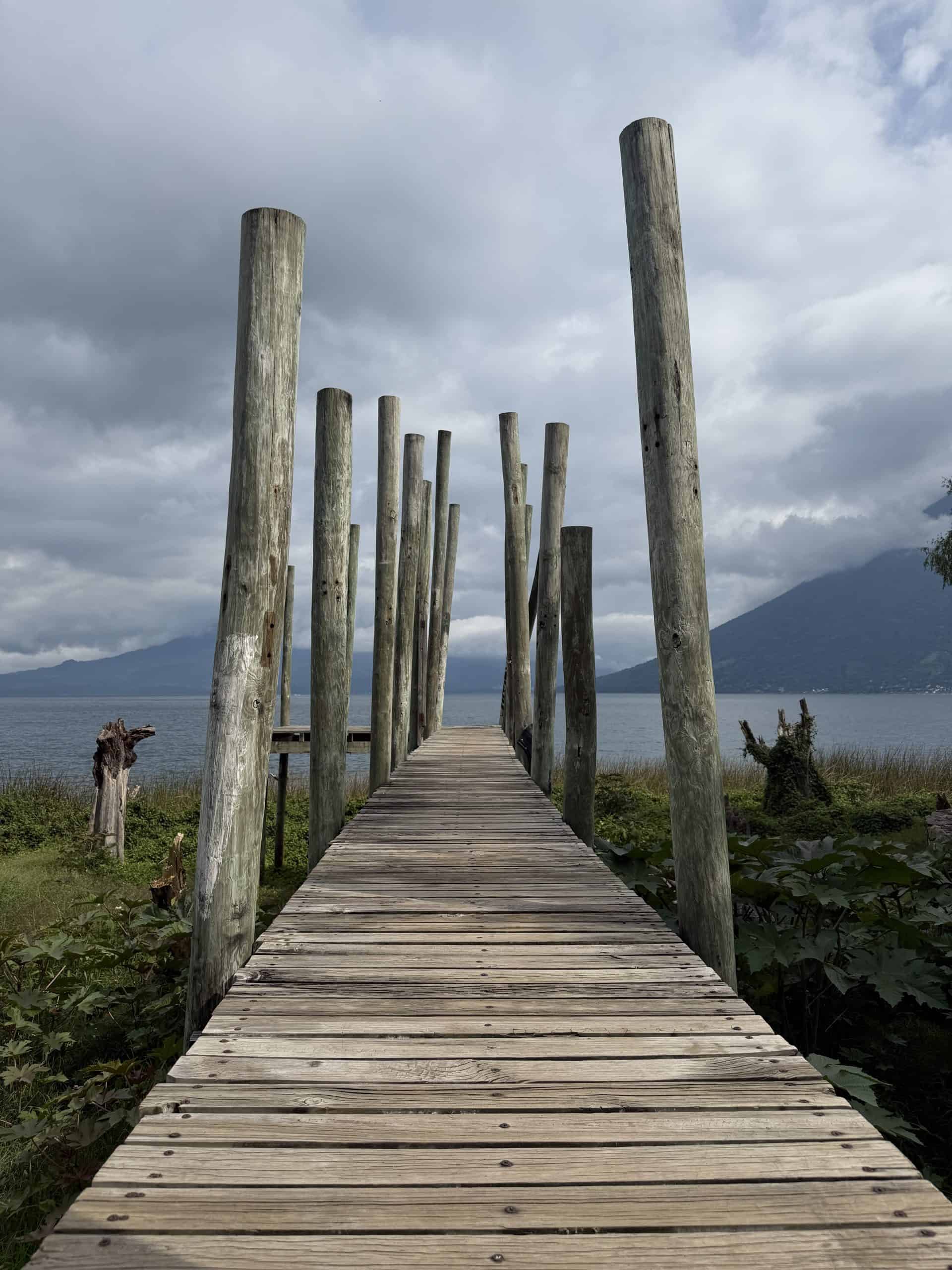 Wooden dock with tall posts leading out over Lake Atitlán under cloudy sky