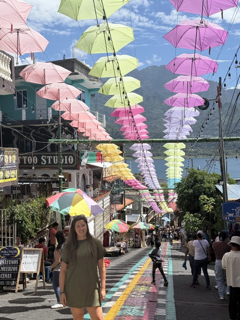 Traveler walking down San Juan La Laguna’s colorful umbrella street with shops and lake view