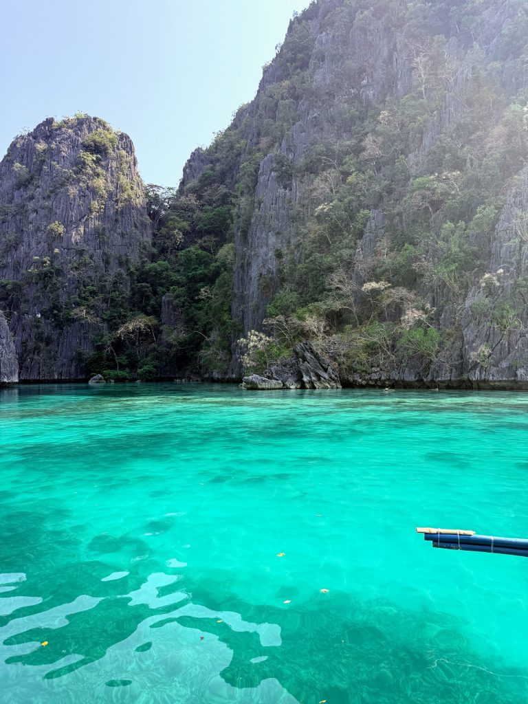Bright turquoise water below steep limestone cliffs at Green Lagoon in Coron, Philippines.