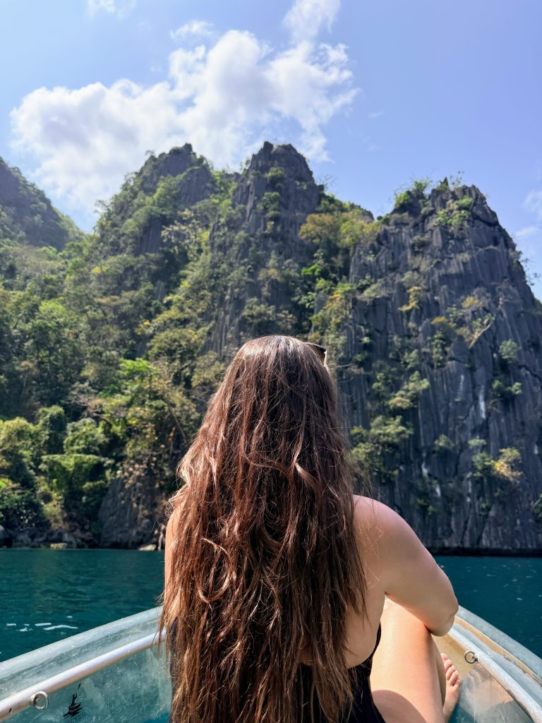 Traveler sitting at the front of a boat facing the limestone cliffs at Twin Lagoon in Coron, Philippines.