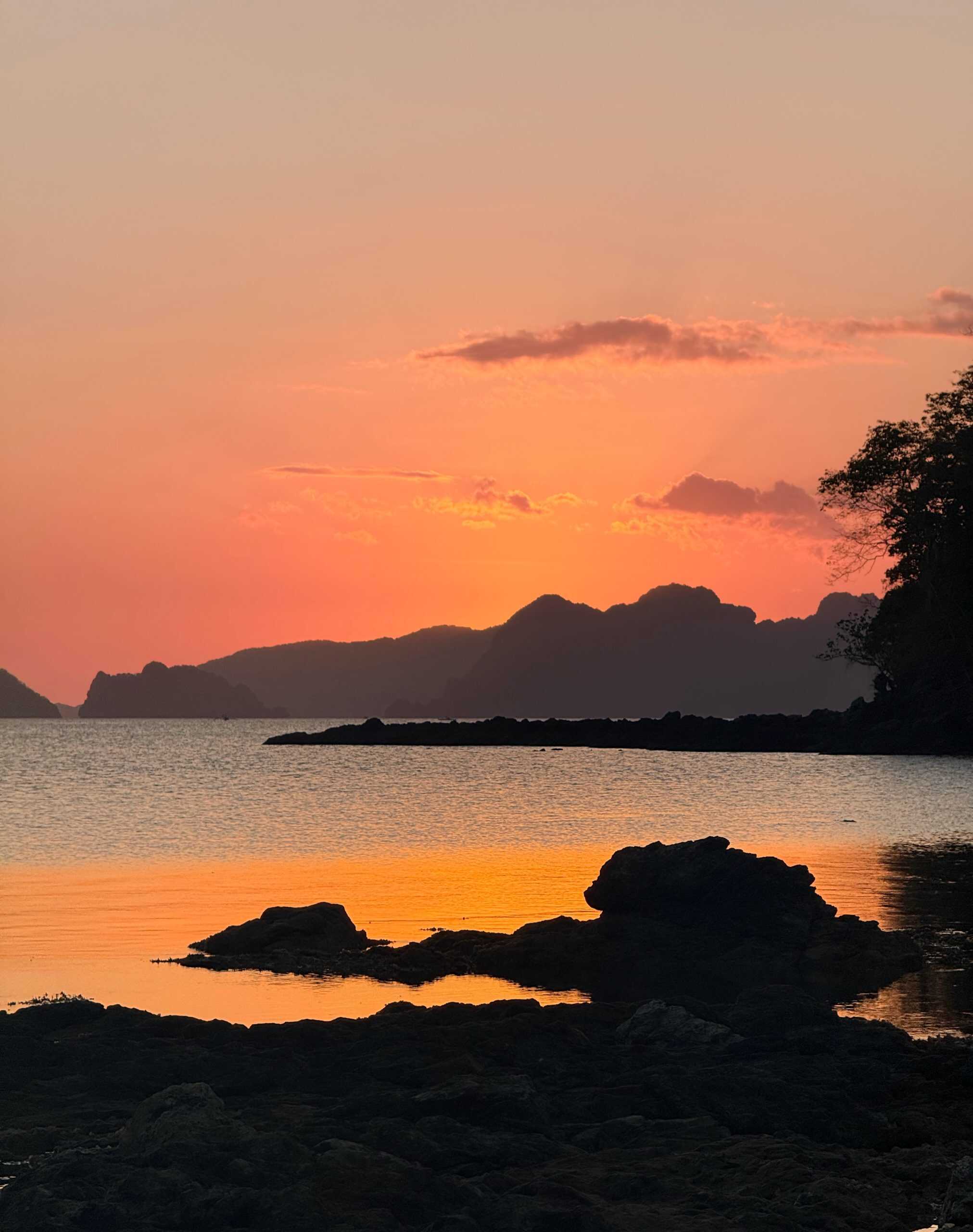 Orange sunset over the sea and rocky shoreline at Las Cabanas in El Nido, Palawan, Philippines.