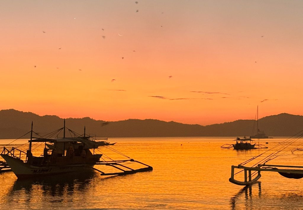 Sunset over the water with traditional boats in Port Barton, Palawan, Philippines.
