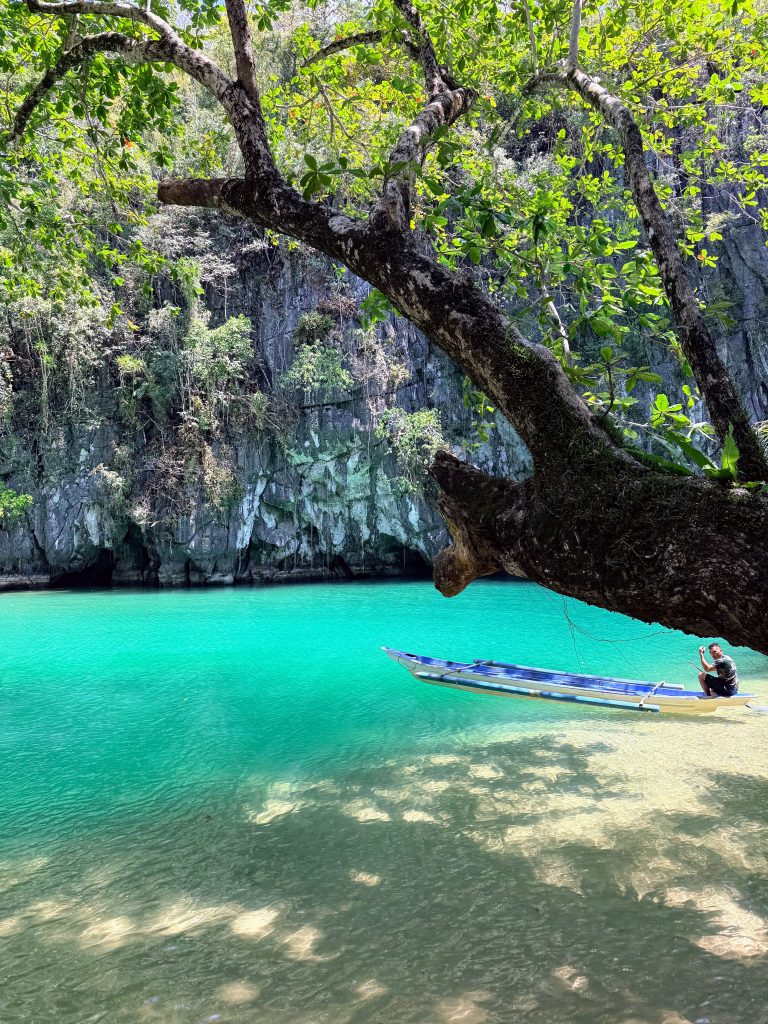 Turquoise lagoon with a leaning tree and small boat at Puerto Princesa Subterranean River National Park in Palawan, Philippines.