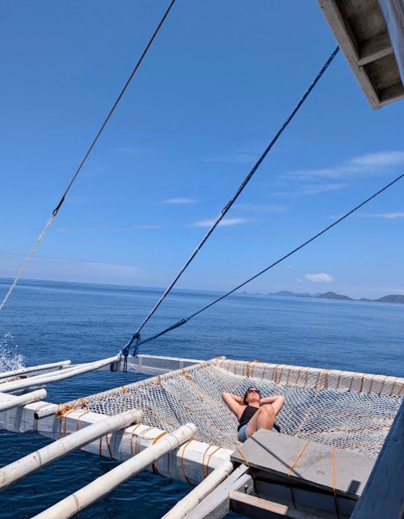 Traveler relaxing on the front boat net during the Sea Expedition from El Nido to Coron, Philippines.