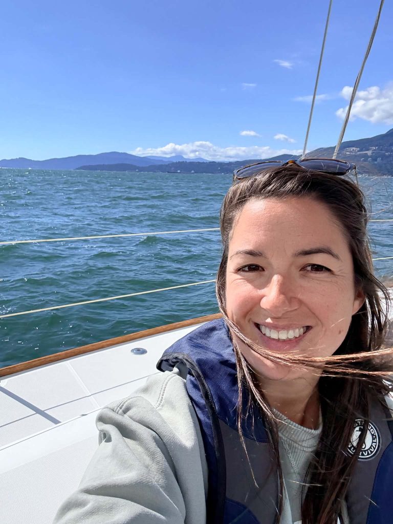 Annie smiling on a sailboat in English Bay, Vancouver with ocean and mountains in the background