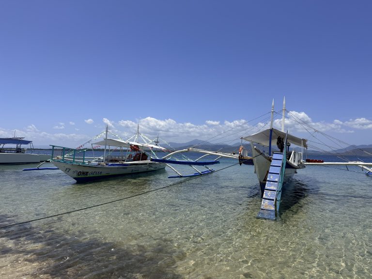Clear shallow water sandy beach and boats at Starfish Island during Honda Bay island hopping in Puerto Princesa, Philippines.