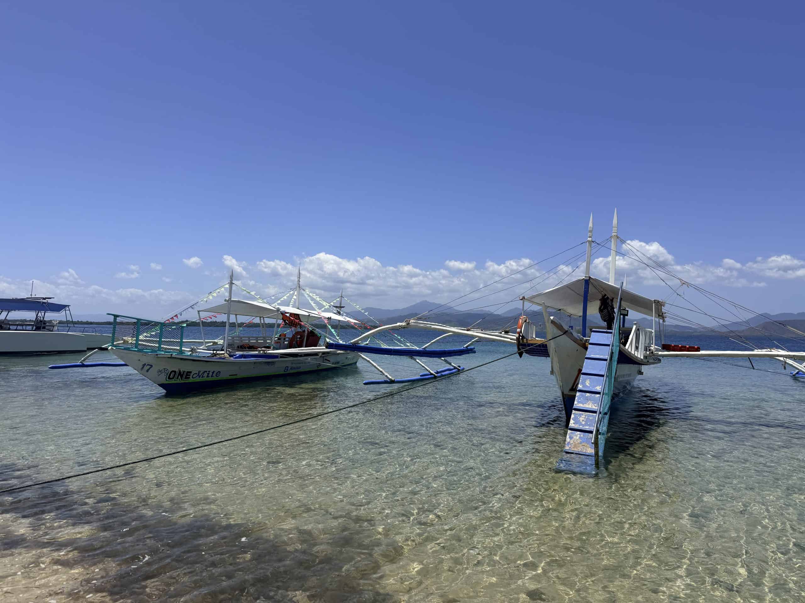 Clear shallow water sandy beach and boats at Starfish Island during Honda Bay island hopping in Puerto Princesa, Philippines.