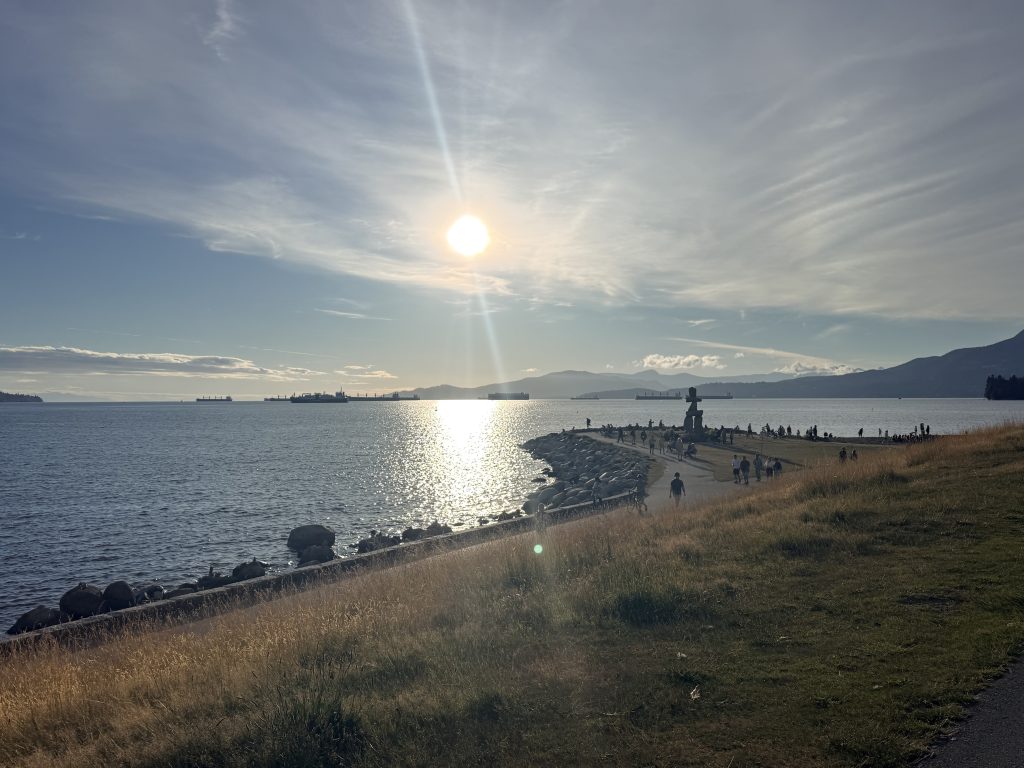 Sunset over English Bay with the Vancouver Inukshuk, mountains and cargo ships along the horizon.