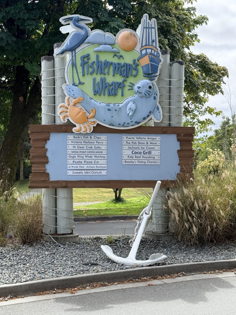 Fisherman’s Wharf entrance sign in Victoria with a seal illustration and nearby business listings.