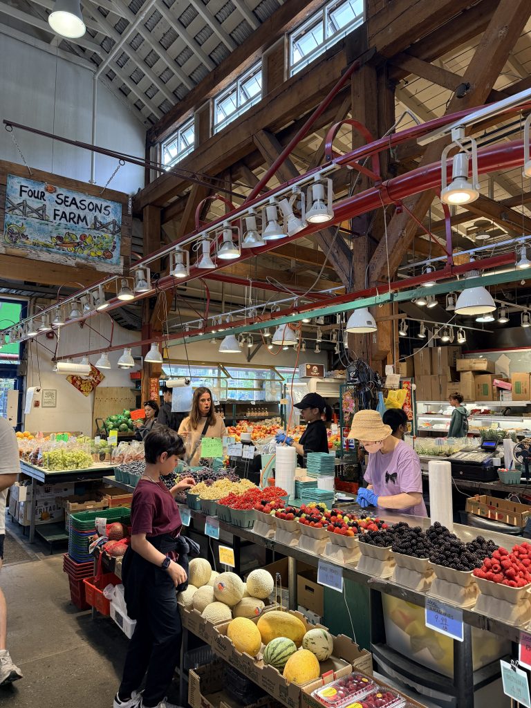 Busy produce stall with berries and melons inside Granville Island Public Market.