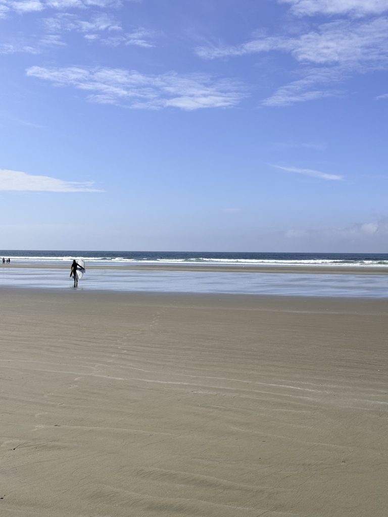 Surfer walking across the wide sandy shoreline at Long Beach in Pacific Rim National Park Reserve.
