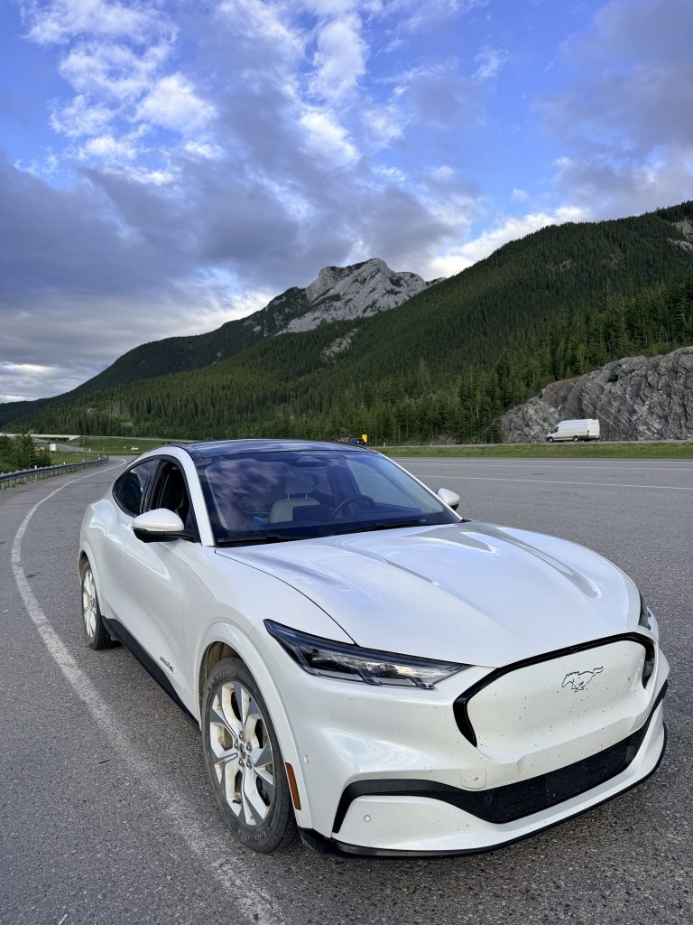 White Ford Mustang Mach-E parked along a mountain highway during a Canadian Rockies road trip in Alberta.