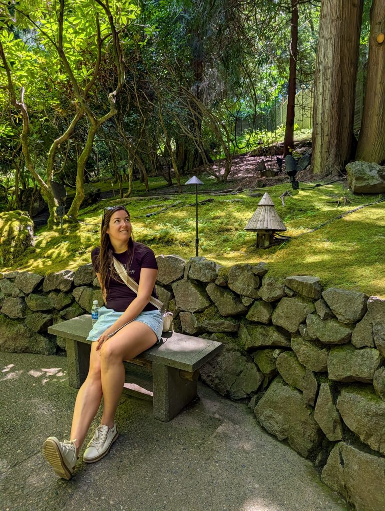 Annie sitting beside a moss-covered landscape in the shaded Japanese Garden at Butchart Gardens.
