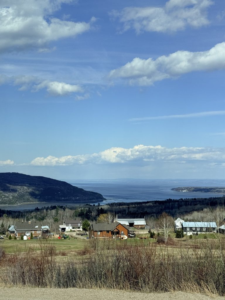 View over Baie-Saint-Paul in Charlevoix with countryside homes, hills and the St. Lawrence River in the distance.