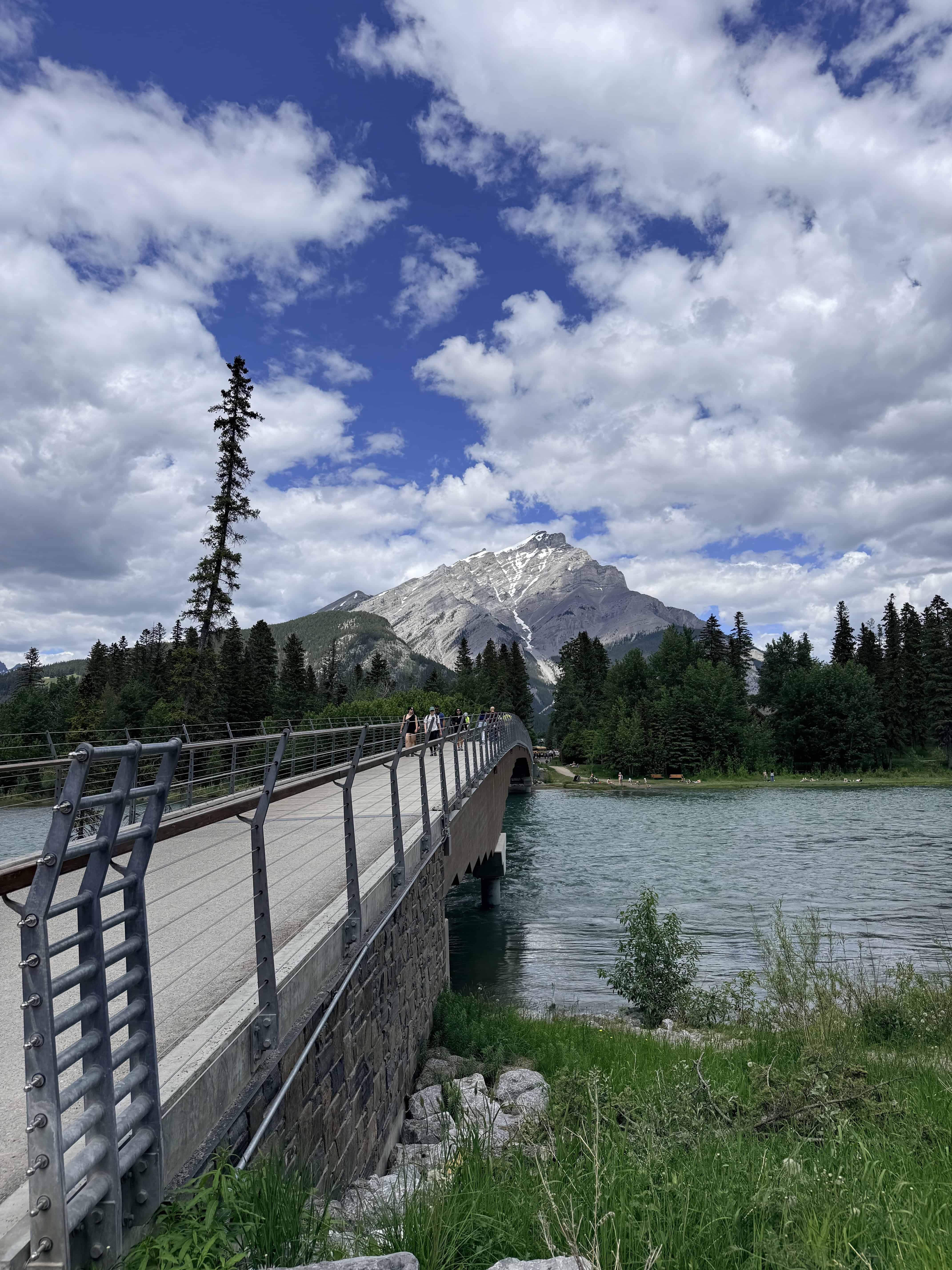 Bow River pedestrian bridge framed by forest and Rocky Mountain scenery in Banff.