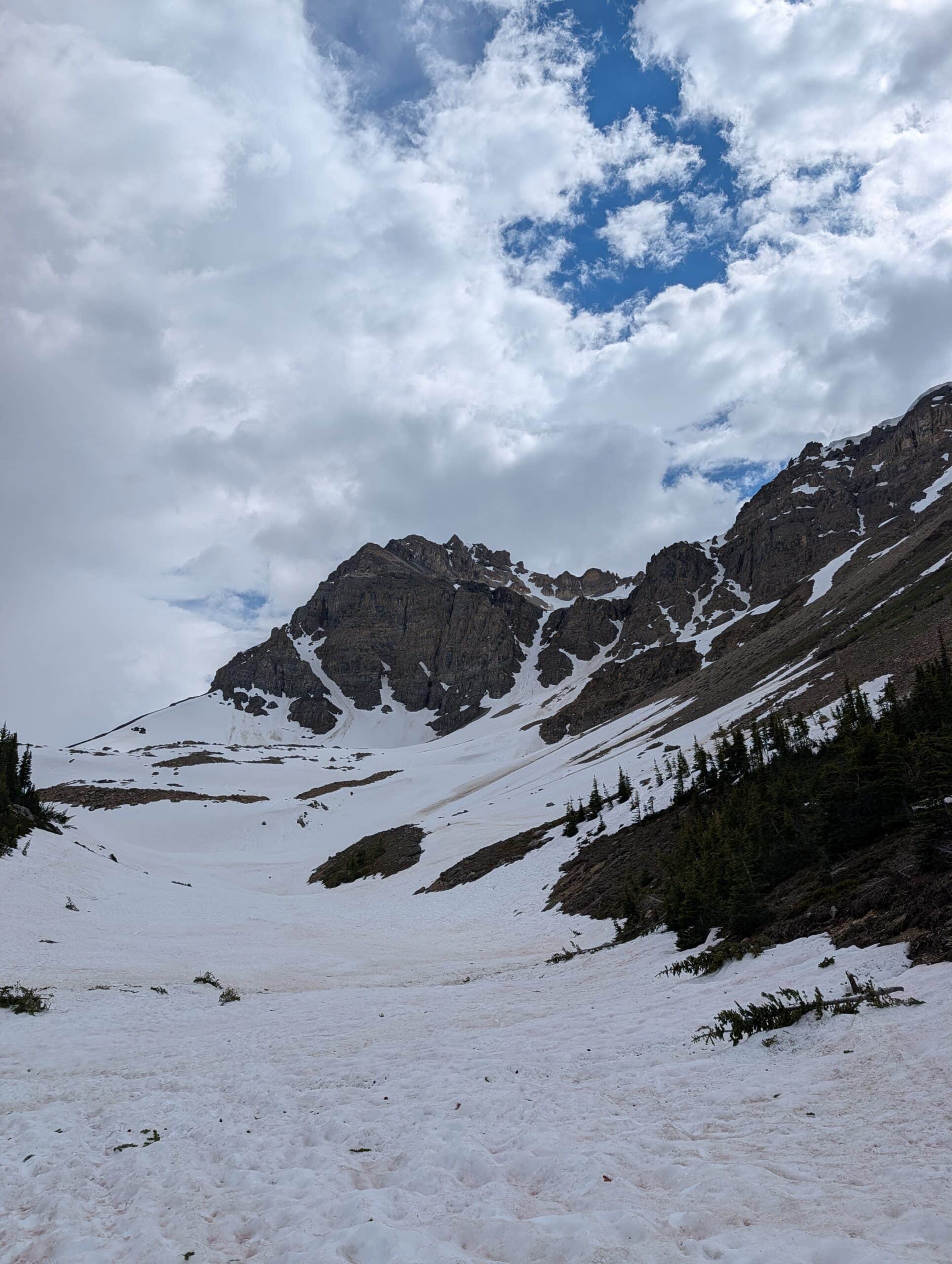 Snow-covered slopes beneath rugged mountain cliffs along the Bow Summit hike in Banff National Park.