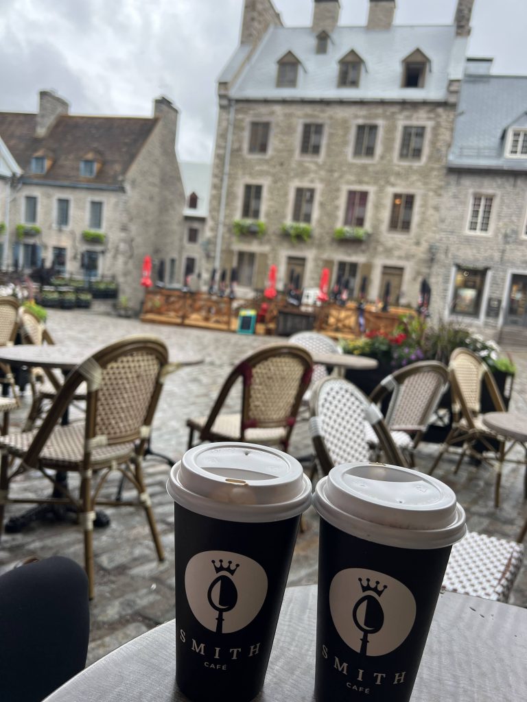 Two Café Smith coffees on a terrace overlooking the historic stone buildings of Place Royale in Old Quebec City.