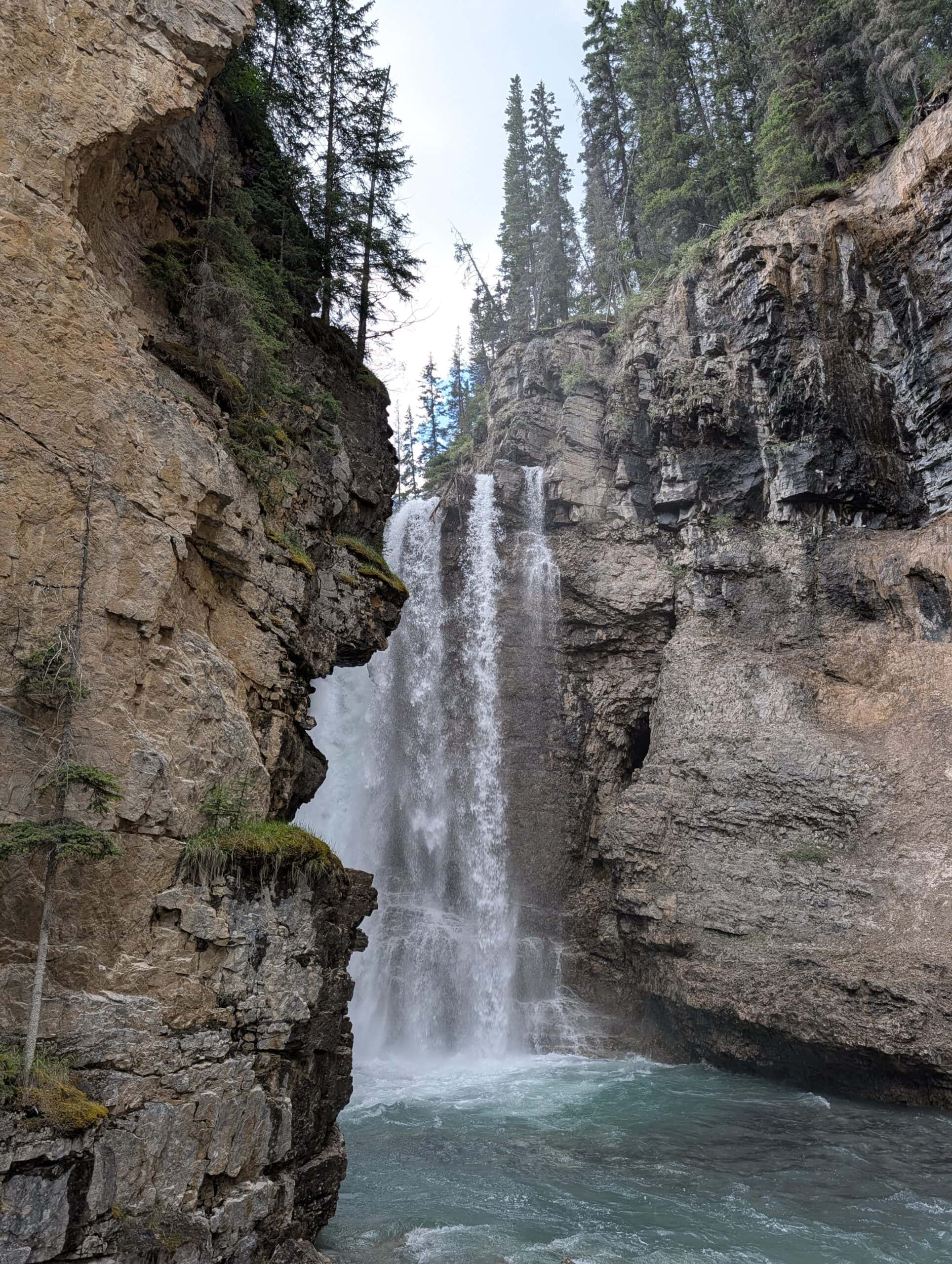 Upper Falls plunging between steep rock walls into a turquoise pool in Johnston Canyon, Banff National Park.