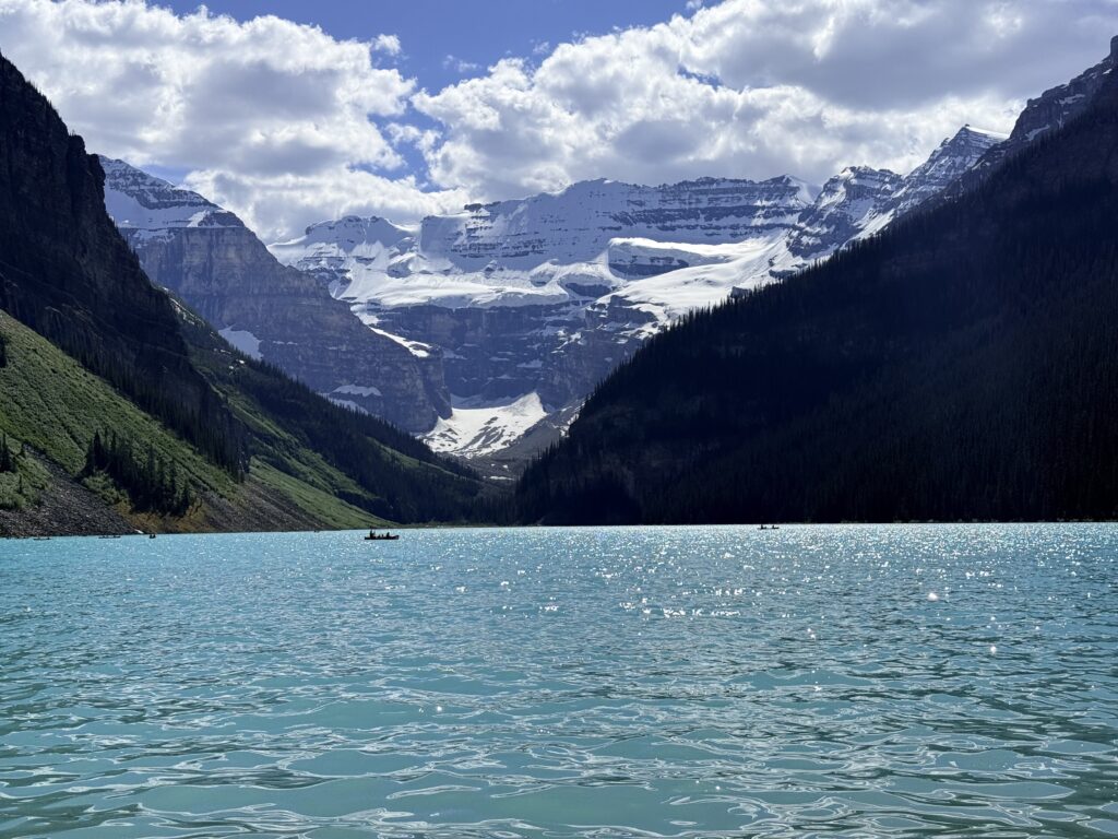 Canoes on turquoise Lake Louise beneath Victoria Glacier and snow-covered mountains, framed by forested slopes in Banff National Park.