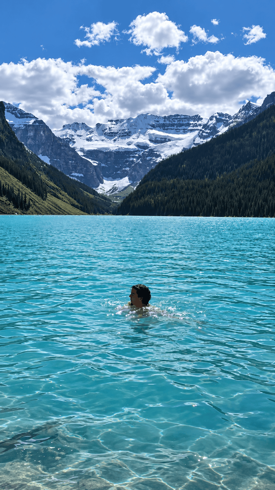 Swimming in turquoise Lake Louise with snow-covered mountains in Banff National Park, Alberta.