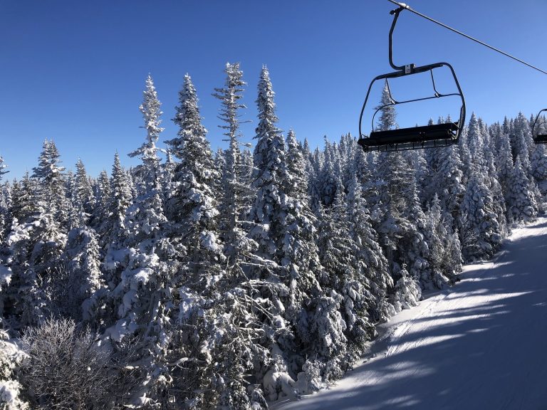 Chairlift above snow-covered forest and ski runs at Massif du Sud on a clear winter day.