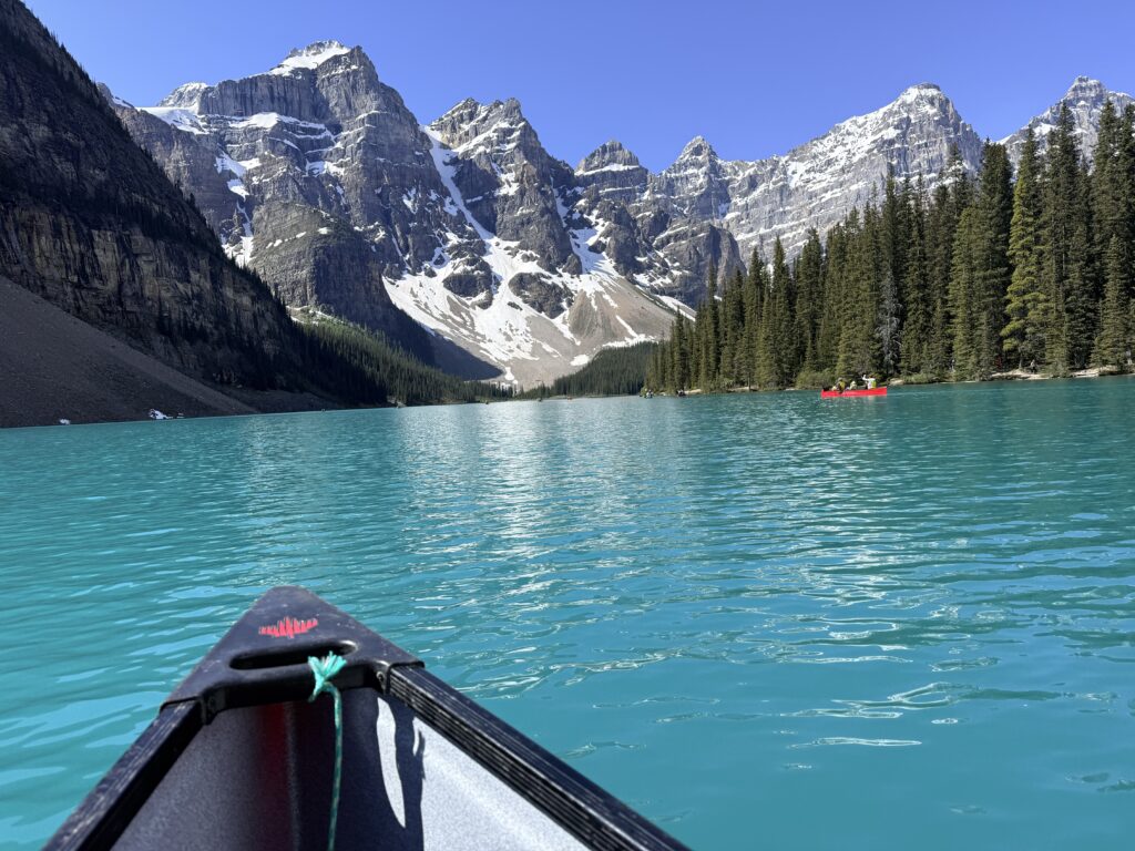 View from a canoe on turquoise Moraine Lake surrounded by snow-covered Rocky Mountain peaks in Banff National Park.