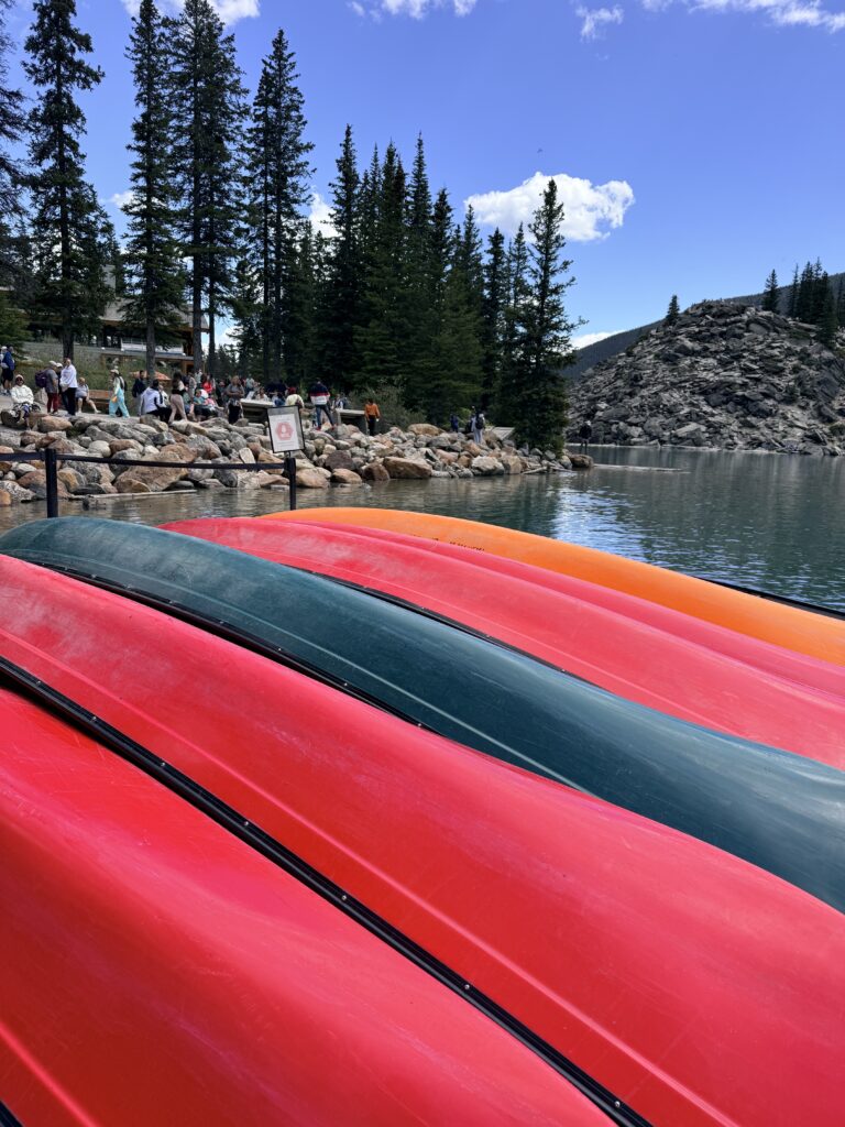 Colorful rental canoes stacked along the shore at Moraine Lake in Banff National Park.