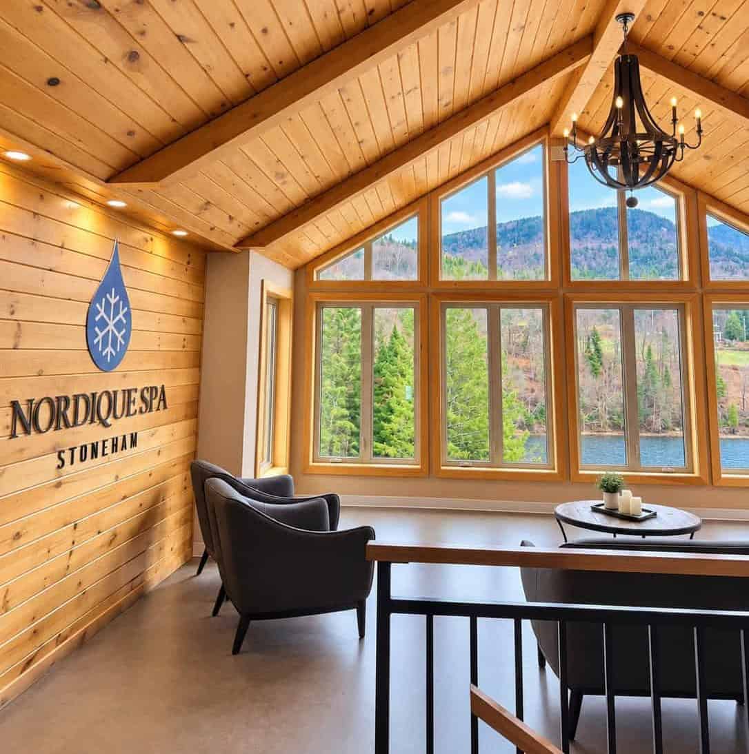 Interior lounge at Nordique Spa Stoneham with wood-paneled walls, large windows and mountain views near Quebec City.
