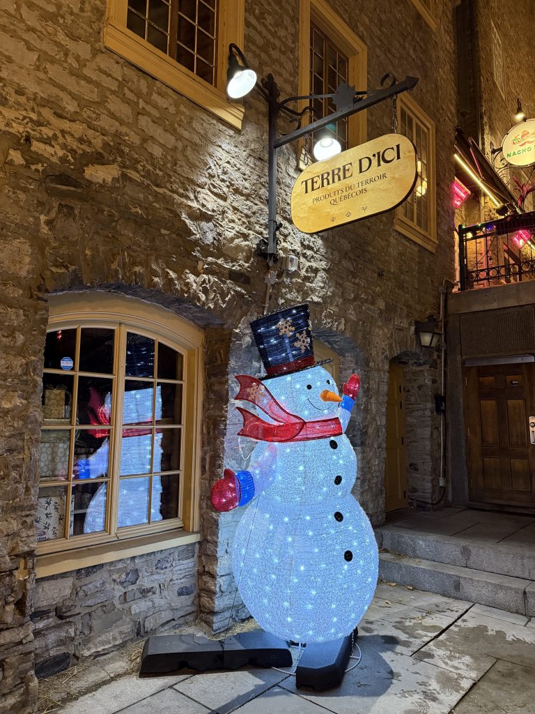 Illuminated snowman decoration beside a stone building in Old Quebec during winter
