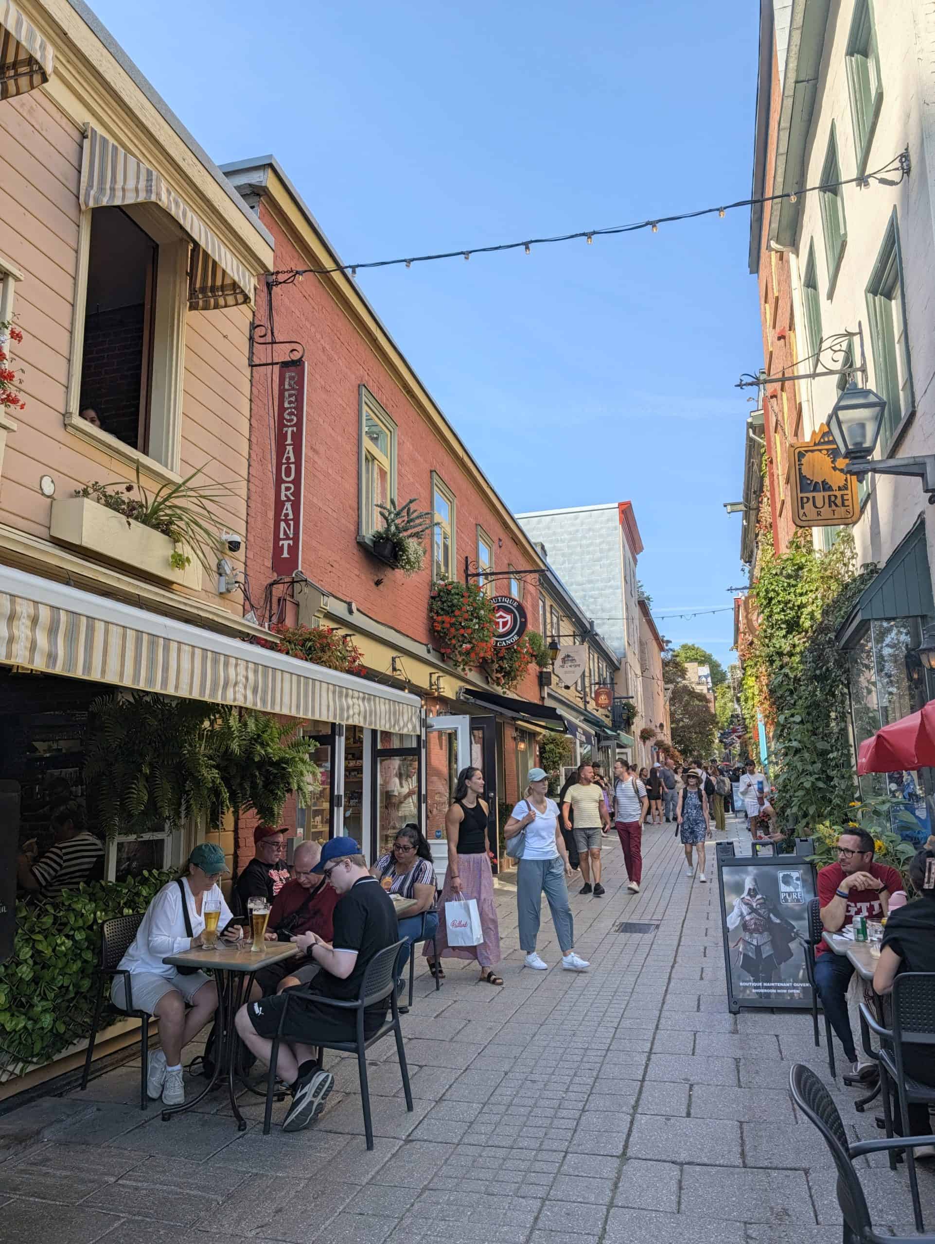 Visitors walking past restaurant patios and colourful historic buildings on Rue du Petit-Champlain in Quebec City.