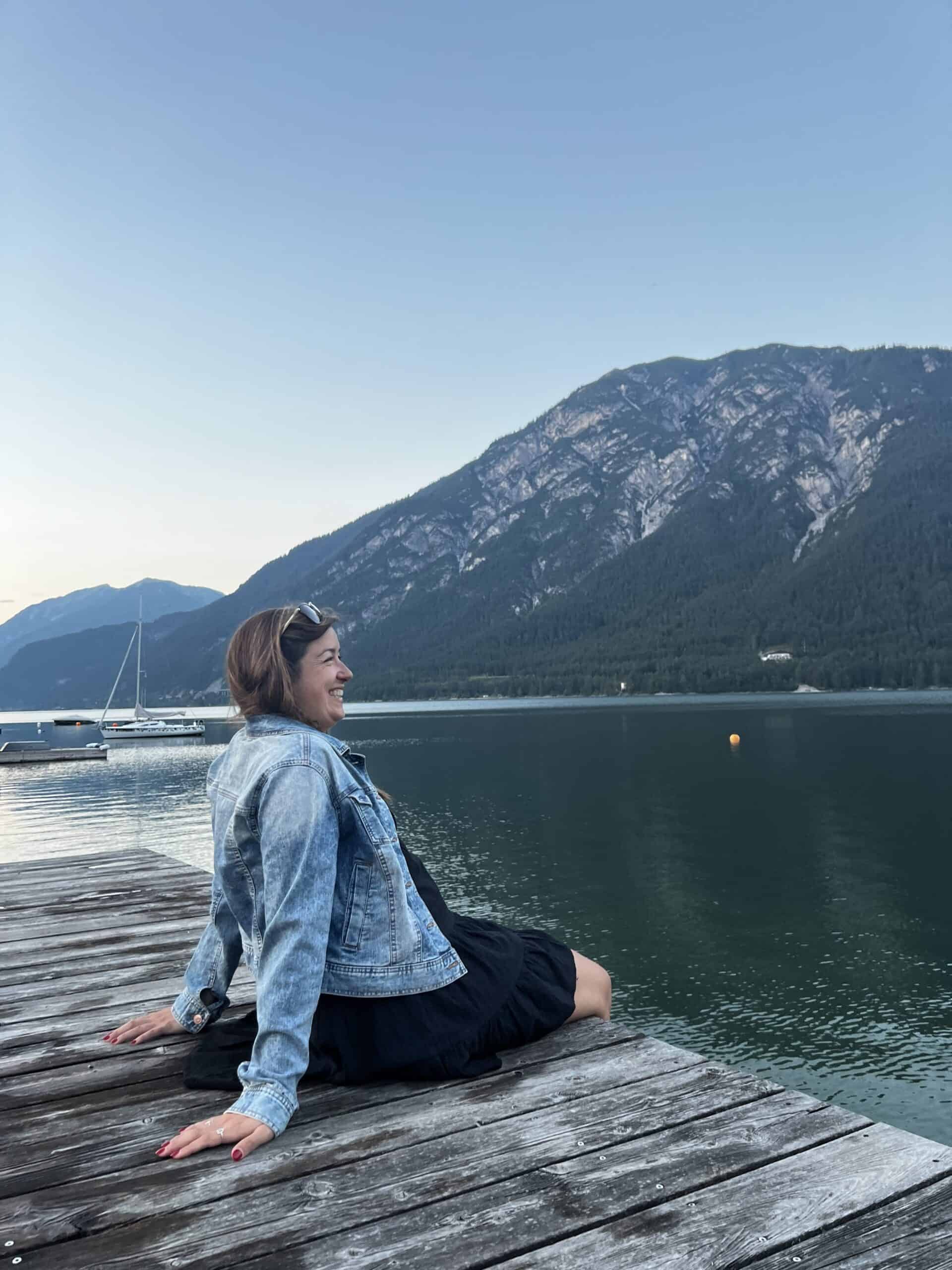 Woman sitting on a wooden dock beside an alpine lake in Austria at sunset