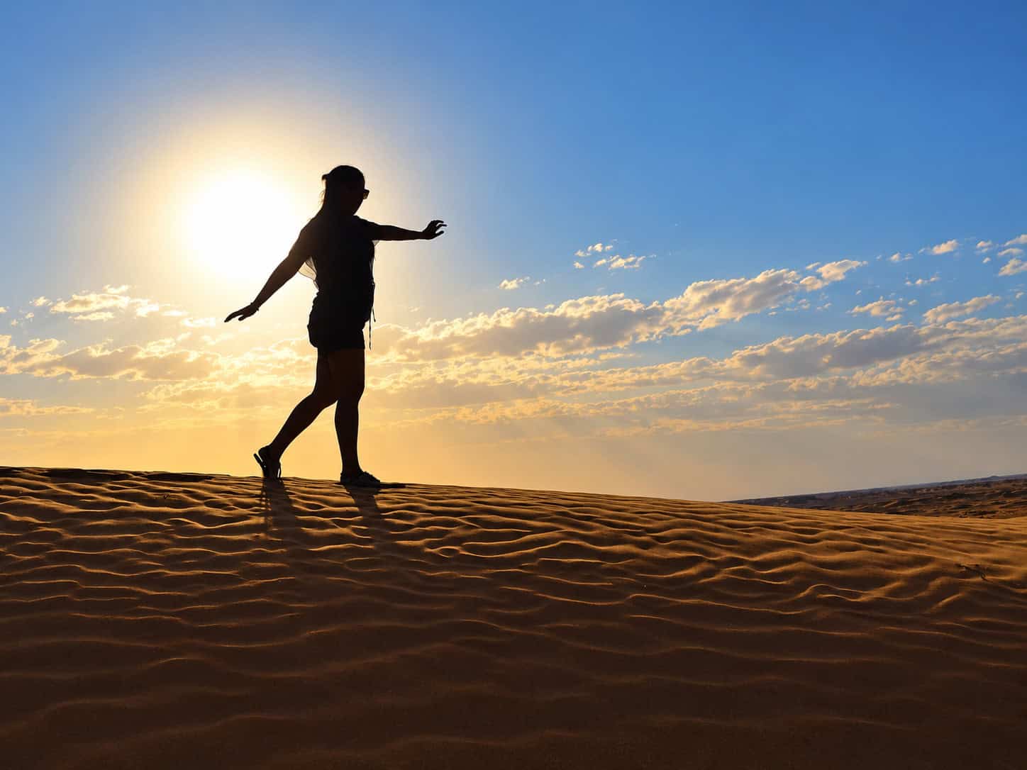 Woman walking alone across Sahara Desert dunes in Morocco at sunset