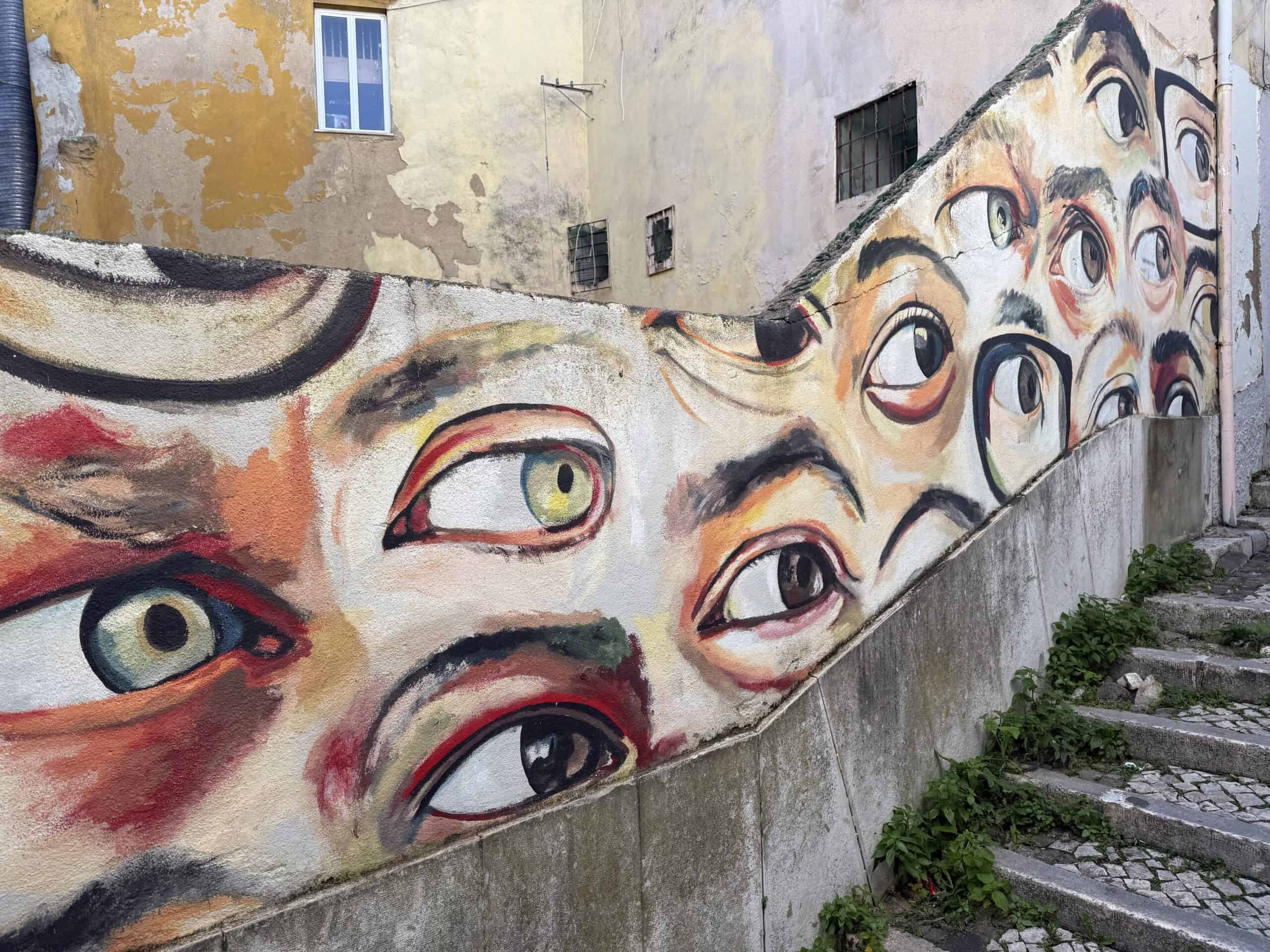 Large street art mural featuring painted eyes on a wall in the historic Alfama neighbourhood of Lisbon.
