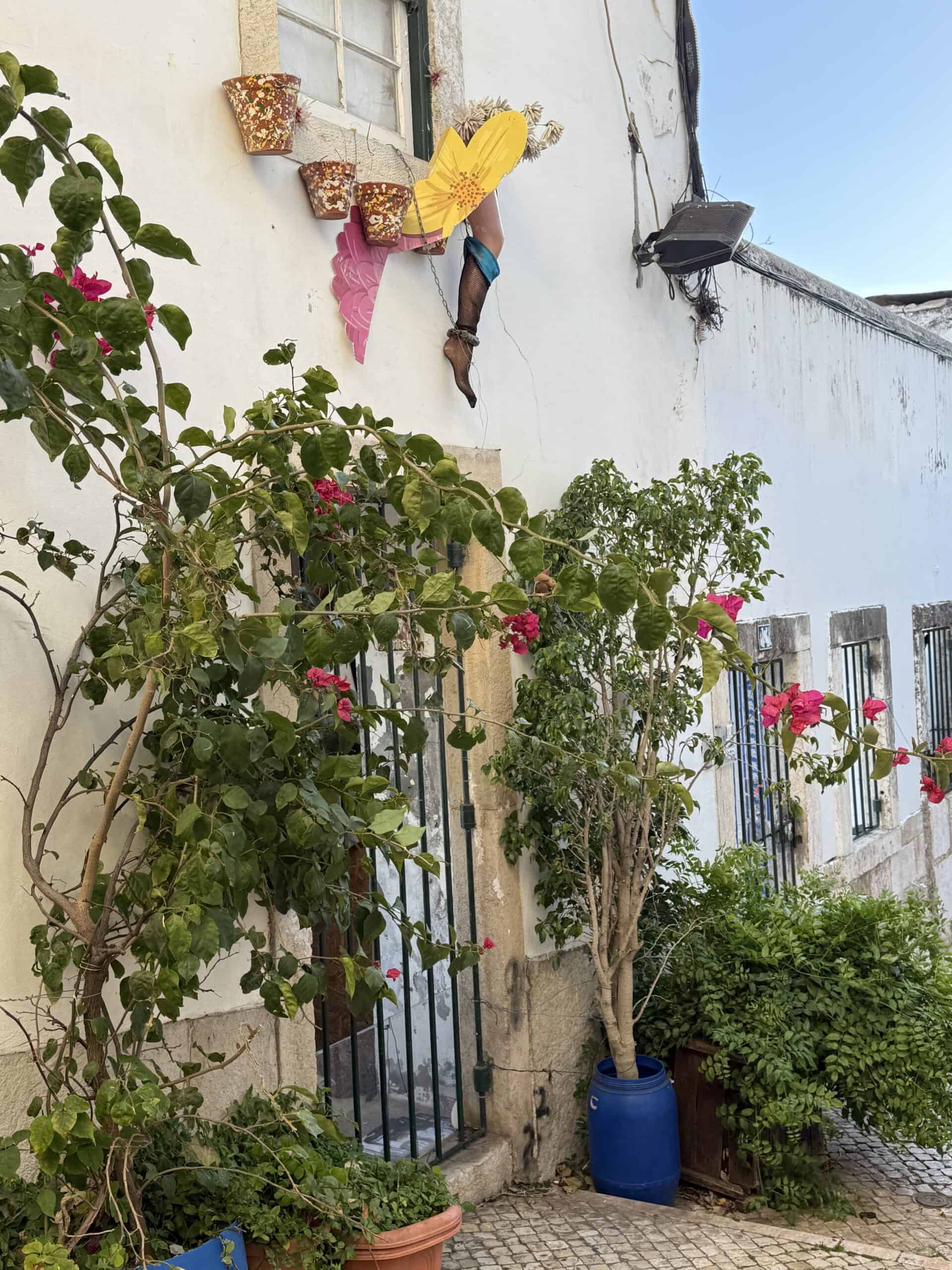 Flowering plants and colourful wall decorations outside a traditional white building in Alfama, Lisbon.