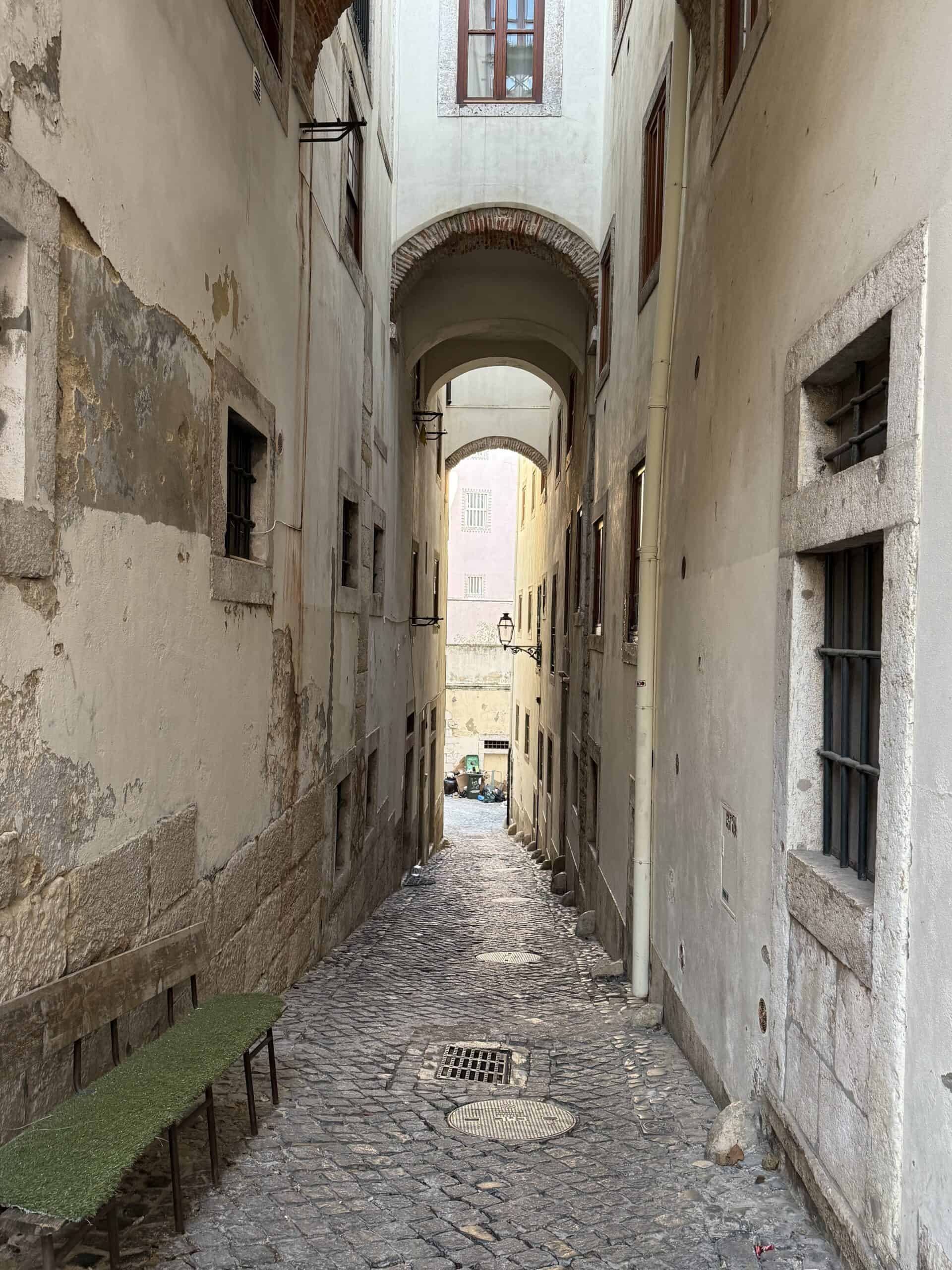 Hidden cobblestone passageway with historic stone and brick arches between old buildings in Alfama, Lisbon.