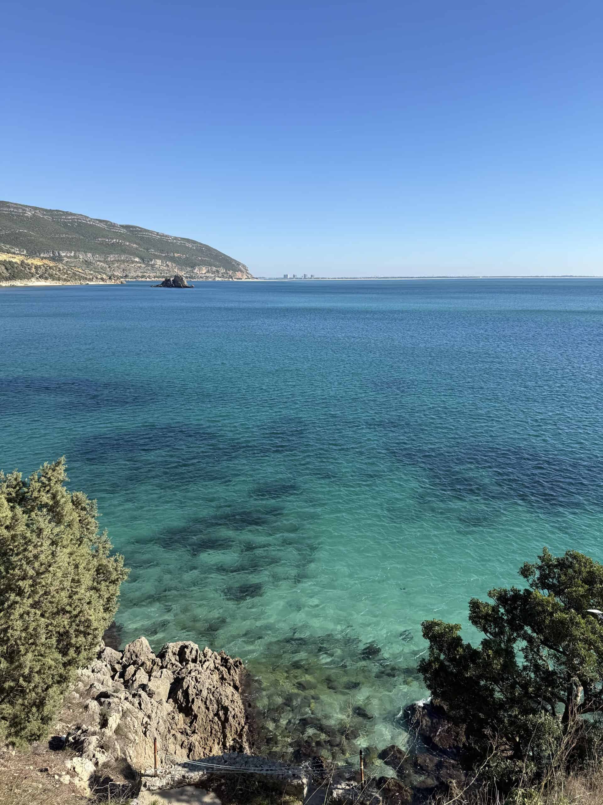 Crystal-clear turquoise water revealing underwater rocks along the rugged coastline of Arrábida Natural Park, Portugal