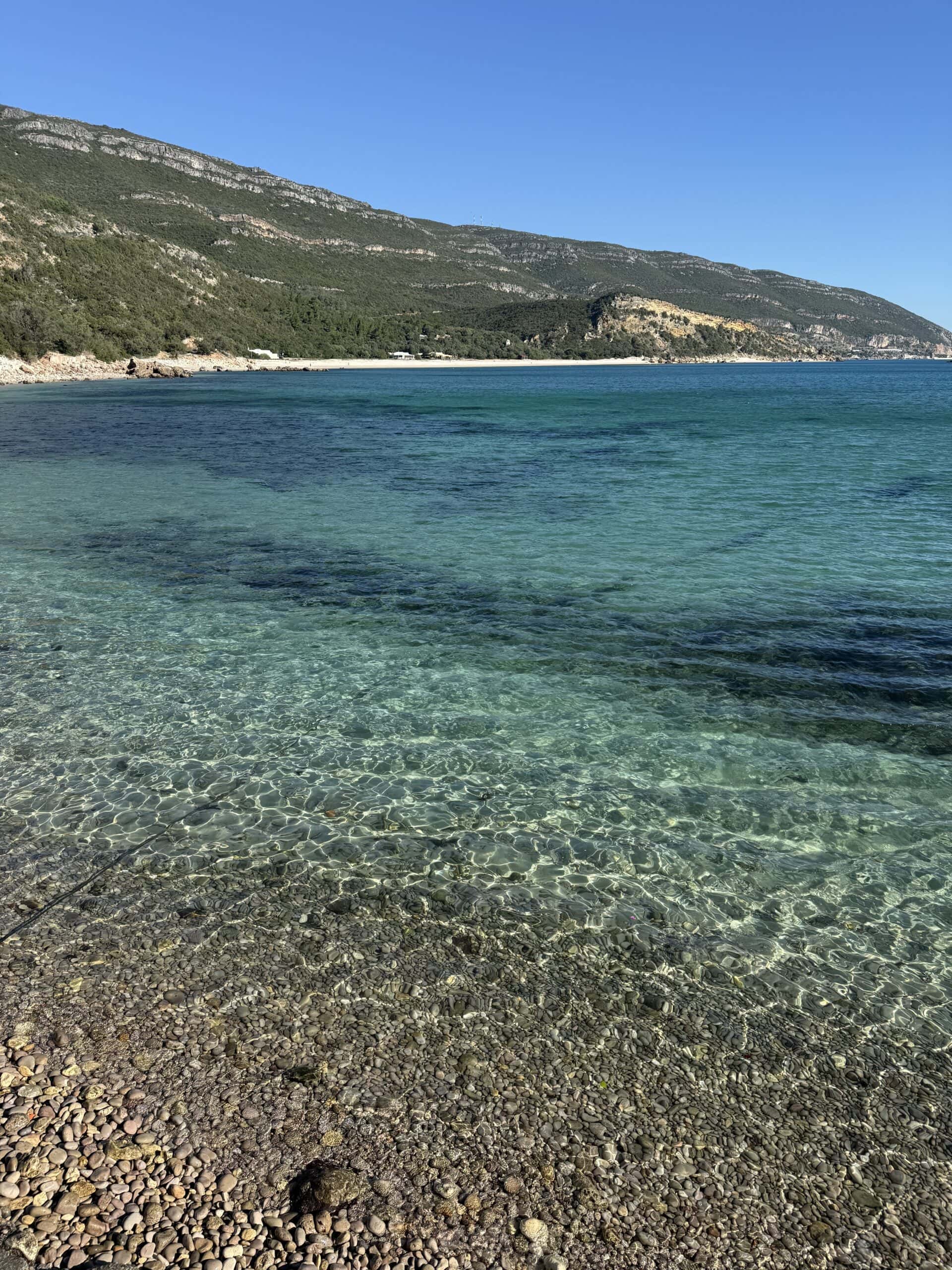 Crystal-clear turquoise water along the green mountainous coastline of Arrábida Natural Park, Portugal