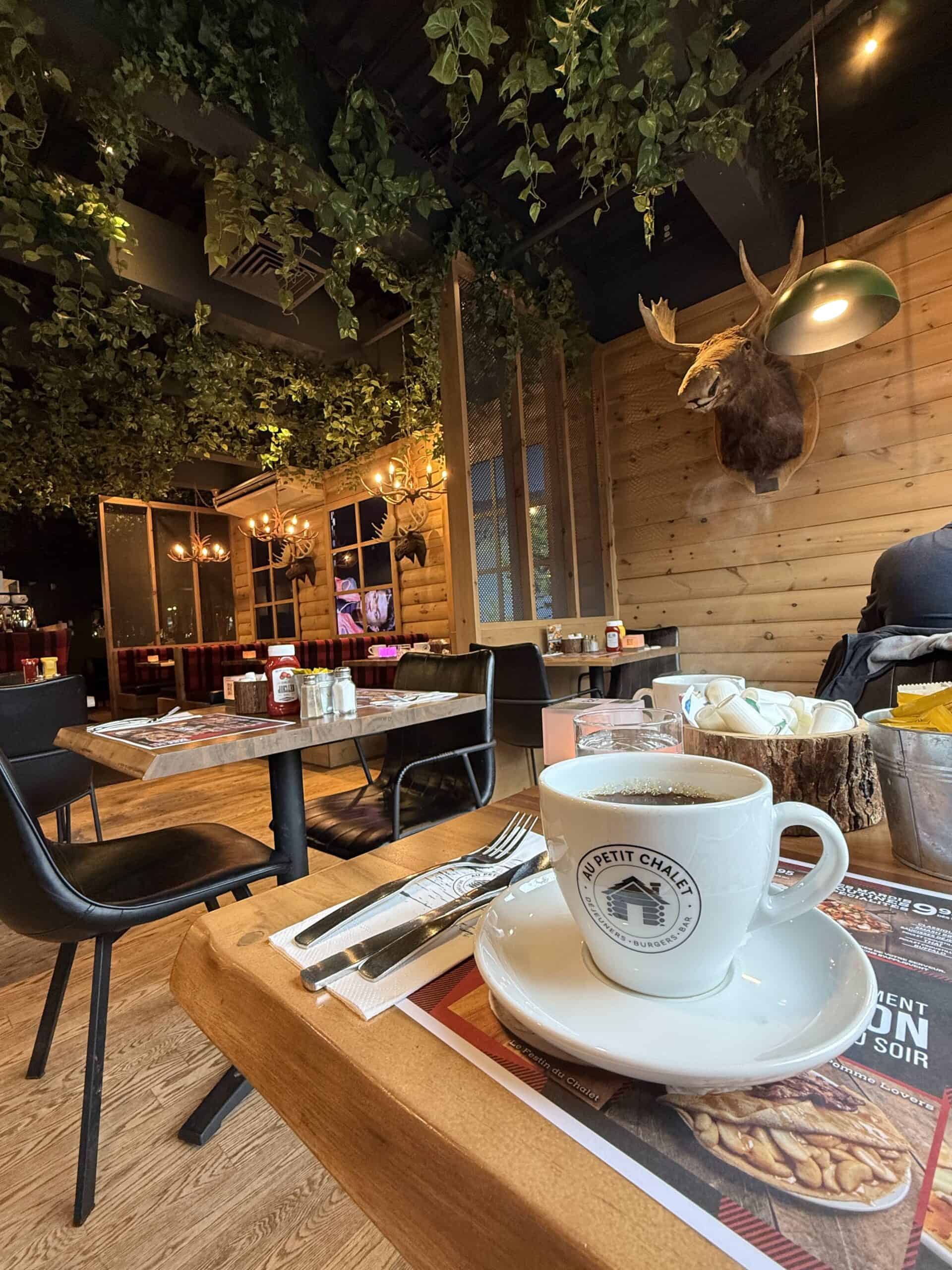 Cozy chalet-style interior of Au Petit Chalet on Maguire in Quebec City, featuring wooden decor, hanging greenery and a coffee cup.