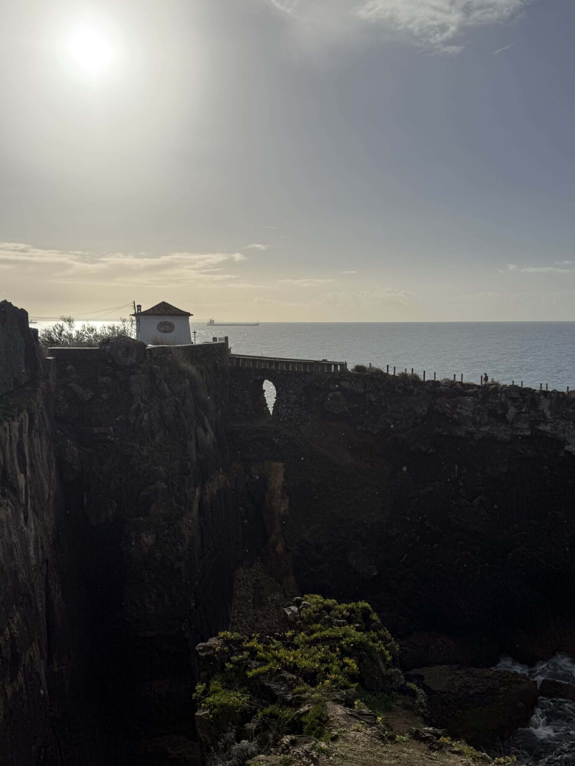 Steep cliffs and a stone viewing terrace above the rocky chasm at Boca do Inferno in Cascais, with the Atlantic Ocean beyond.